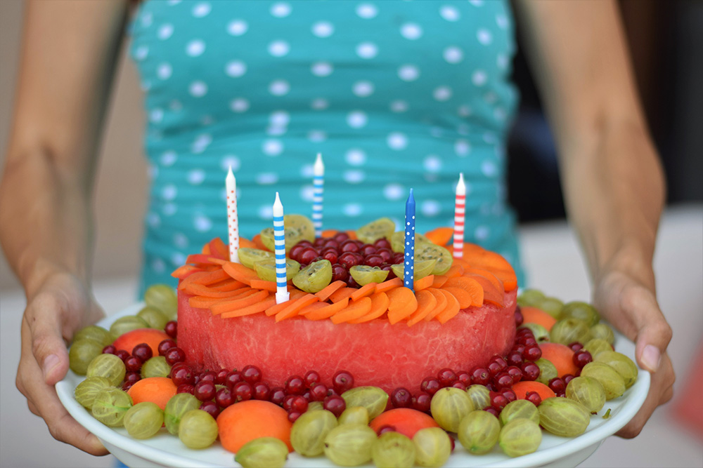 Torta z melóna zdobená ovocím, ktorú nesie dospelá osoba