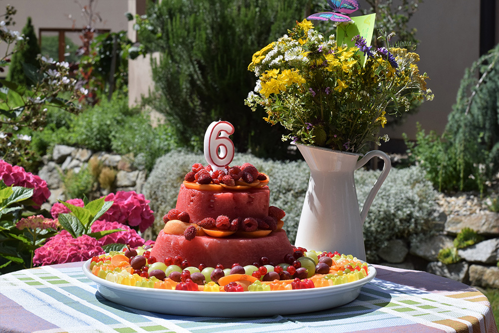 Torta z melóna zdobená ovocím na stole s kyticou vo váze